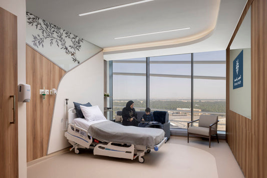Modern hospital patient room at Almoosa Rehabilitation Hospital with a hospital bed, comfortable seating, large window view, and a family visiting – غرفة مريض حديثة في مستشفى الموسى للتأهيل بسرير طبي، ومقاعد مريحة، وإطلالة بانورامية، وزيارة عائلية 4