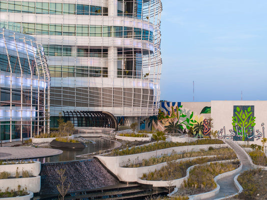 Close-up view of Almoosa Rehabilitation Hospital exterior featuring modern architecture, tiered landscaping, flowing water feature, and Arabic mural art – منظر خارجي قريب لمستشفى الموسى للتأهيل بتصميم معماري عصري، وحدائق متدرجة، ونافورة مائية جارية، وفن جداري عربي 3