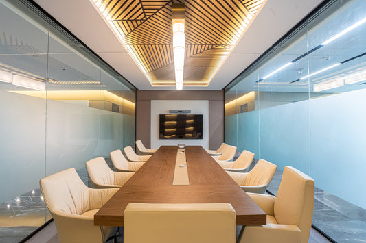 Modern conference room with long wooden table, cream leather chairs, glass partitions, and geometric ceiling lighting by Atelier 21 KSA, top office furniture supplier in Riyadh – غرفة اجتماعات عصرية تحتوي على طاولة خشبية طويلة، كراسي جلدية كريمية، فواصل زجاجية، وإضاءة سقفية هندسية من تصميم مفن الرسام، أفضل مورّد أثاث مكتبي في الرياض 13
