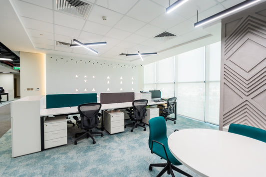 Open-plan modern office with ergonomic chairs, shared workstations, and geometric wall design by Atelier 21 KSA, top office furniture supplier in Riyadh – مكتب مفتوح عصري يحتوي على كراسي مريحة، محطات عمل مشتركة، وجدار بزخارف هندسية من تصميم مفن الرسام، أفضل مورّد أثاث مكتبي في الرياض 15