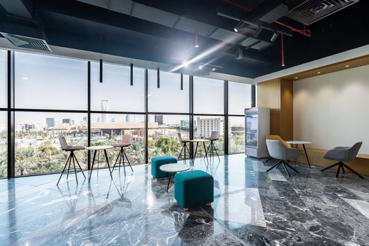 Modern office break area with panoramic Riyadh skyline view, high-top tables, soft seating, and sleek marble flooring – designed by Atelier 21 KSA for the Ministry of Municipal and Rural Affairs and Housing – منطقة استراحة مكتبية عصرية بإطلالة بانورامية على أفق الرياض، طاولات عالية، مقاعد مريحة، وأرضيات رخامية أنيقة – من تصميم مفن الرسام لوزارة الشؤون البلدية والإسكان 29