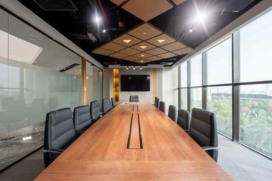 Modern conference room with long wooden meeting table, black leather chairs, indoor plants, and wall-mounted screen by Atelier 21 KSA, top office furniture supplier in Riyadh – غرفة اجتماعات عصرية تحتوي على طاولة اجتماعات خشبية طويلة، كراسي جلدية سوداء، نباتات داخلية، وشاشة مثبتة على الحائط من تصميم مفن الرسام، أفضل مورّد أثاث مكتبي في الرياض 22