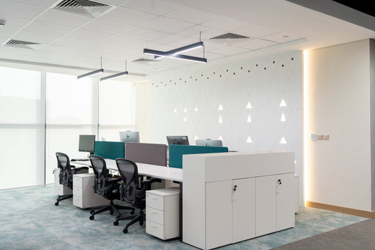 Minimalist open-plan office with white desks, ergonomic chairs, modern lighting, and geometric wall design by Atelier 21 KSA, leading office interior design firm and workspace furniture supplier in Saudi Arabia – مكتب مفتوح بتصميم بسيط يشمل مكاتب بيضاء، كراسي مريحة، إضاءة عصرية، وجدار هندسي من تنفيذ مفن الرسام، الرائد في تصميم المكاتب وتوريد الأثاث المكتبي في السعودية 25