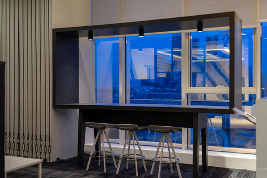 Modern high table setup in a Tawal office corner, featuring a sleek black bar table with three minimalist stools, built-in overhead lighting, and floor-to-ceiling windows offering a city skyline view. Perfect for short breaks or informal meetings. Designed and executed by Atelier 21 KSA.
زاوية مكتبية حديثة في تــوال، تضم طاولة عالية بلون أسود أنيق مع ثلاث مقاعد بسيطة، وإضاءة مدمجة، ونوافذ كبيرة بإطلالة حضرية رائعة. مثالية للاستراحات أو الاجتماعات السريعة – تنفيذ مفن الرسام، أفضل شركة تصميم داخلي في السعودية 11