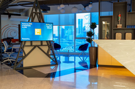 TAWAL headquarters reception area in Riyadh, featuring a bold sculptural desk, digital signage displaying “Great Place to Work,” and skyline views of King Abdullah Financial District – modern interior by Atelier 21, leading fit-out company in KSA.
منطقة استقبال مقر TAWAL في الرياض، بتصميم عصري يشمل مكتب استقبال فني، شاشة رقمية لجوائز “أفضل بيئة عمل”، وإطلالة على حي الملك عبدالله المالي – بتنفيذ مفن الرسام، شركة التصميم الداخلي الرائدة في السعودية. 9