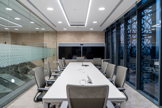 Modern meeting room at the Welaya project in Riyadh, featuring a large white conference table surrounded by ergonomic chairs. The space is enclosed with glass walls and includes a high-tech dual screen for video conferencing. إضاءة حديثة وسقف مدمج تضيف لمسة عصرية على غرفة الاجتماعات في مشروع ولاية بالرياض، طاولة اجتماعات كبيرة، كراسي مريحة، شاشات عرض، تصميم داخلي حديث يدعم بيئة عمل احترافية. 6