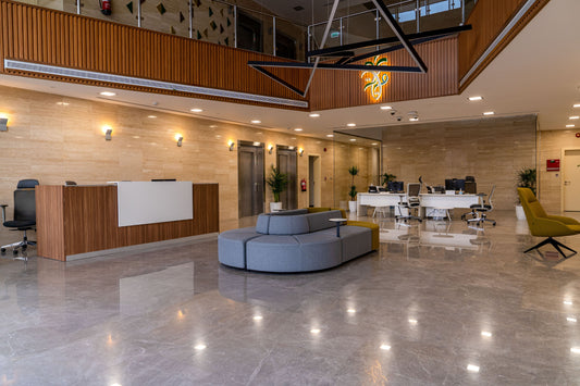 Modern reception area in Riyadh for a government or corporate office, featuring a sleek wooden reception desk, modular grey seating, and marble flooring. Elegant lighting, natural tones, and indoor plants enhance the welcoming design. منطقة استقبال أنيقة في الرياض، تضم مكتب استقبال خشبي، جلسات مريحة، أرضية رخامية، وكراسي مكتبية دوارة. تصميم داخلي حديث لمكاتب حكومية أو شركات خاصة في السعودية. 1