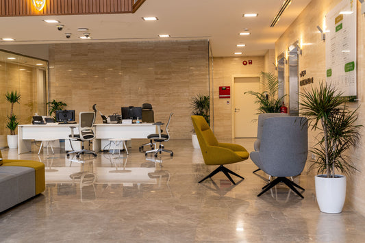 Modern reception area in Welaya project, Riyadh, featuring white workstations, ergonomic office chairs, and accent lounge chairs in olive and grey. The space is enhanced by beige marble walls, polished floors, and decorative indoor plants. تصميم استقبال حديث في مشروع الولاية بالرياض يشمل مكاتب استقبال بيضاء، كراسي مكتبية مريحة، كراسي انتظار أنيقة، أرضيات رخامية، ونباتات داخلية تعزز من بيئة العمل الرسمية. 4