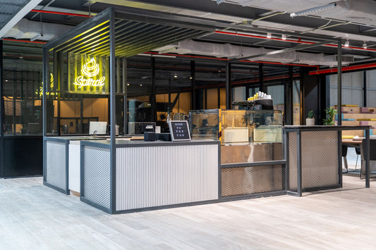 Modern coffee counter at Misk Foundation in Riyadh, featuring a sleek industrial design with black metal framing and ribbed paneling. The setup includes a yellow neon
