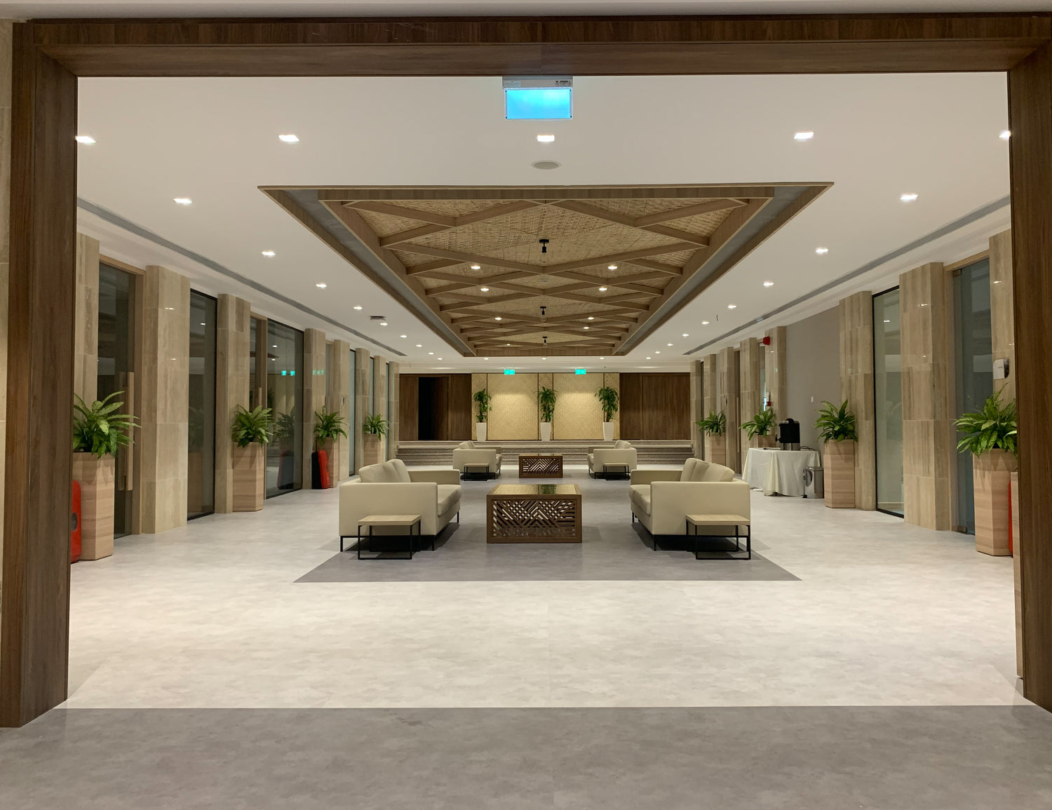 Spacious Majlis-style lounge designed with wooden ceiling details, marble columns, neutral seating, and indoor plants – executed by Atelier 21 KSA, Top Interior Designer and Furniture Supplier in Saudi Arabia and Riyadh. صالة مجلس واسعة بتفاصيل خشبية في السقف وأعمدة رخامية ومقاعد حيادية ونباتات داخلية من تنفيذ مفن الرسام، مما يعكس تميّز مفن الرسام كأفضل مصمم داخلي ومورد أثاث ومصمم مكاتب في السعودية والرياض.