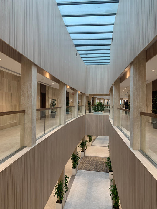 Double-height atrium at The Saudi Irrigation Organization featuring a central skylight, natural stone finishes, and glass balustrades – delivered by Atelier 21 KSA, Top Interior Designer, Fit-out Company, and Furniture Supplier in Saudi Arabia and Riyadh. بهو داخلي بارتفاع مزدوج في المؤسسة العامة للري، مع سقف زجاجي وتشطيبات حجرية طبيعية وحواجز زجاجية، من تنفيذ مفن الرسام، كأفضل شركة تصميم داخلي وتنفيذ تشطيبات ومورد أثاث في السعودية والرياض. 4