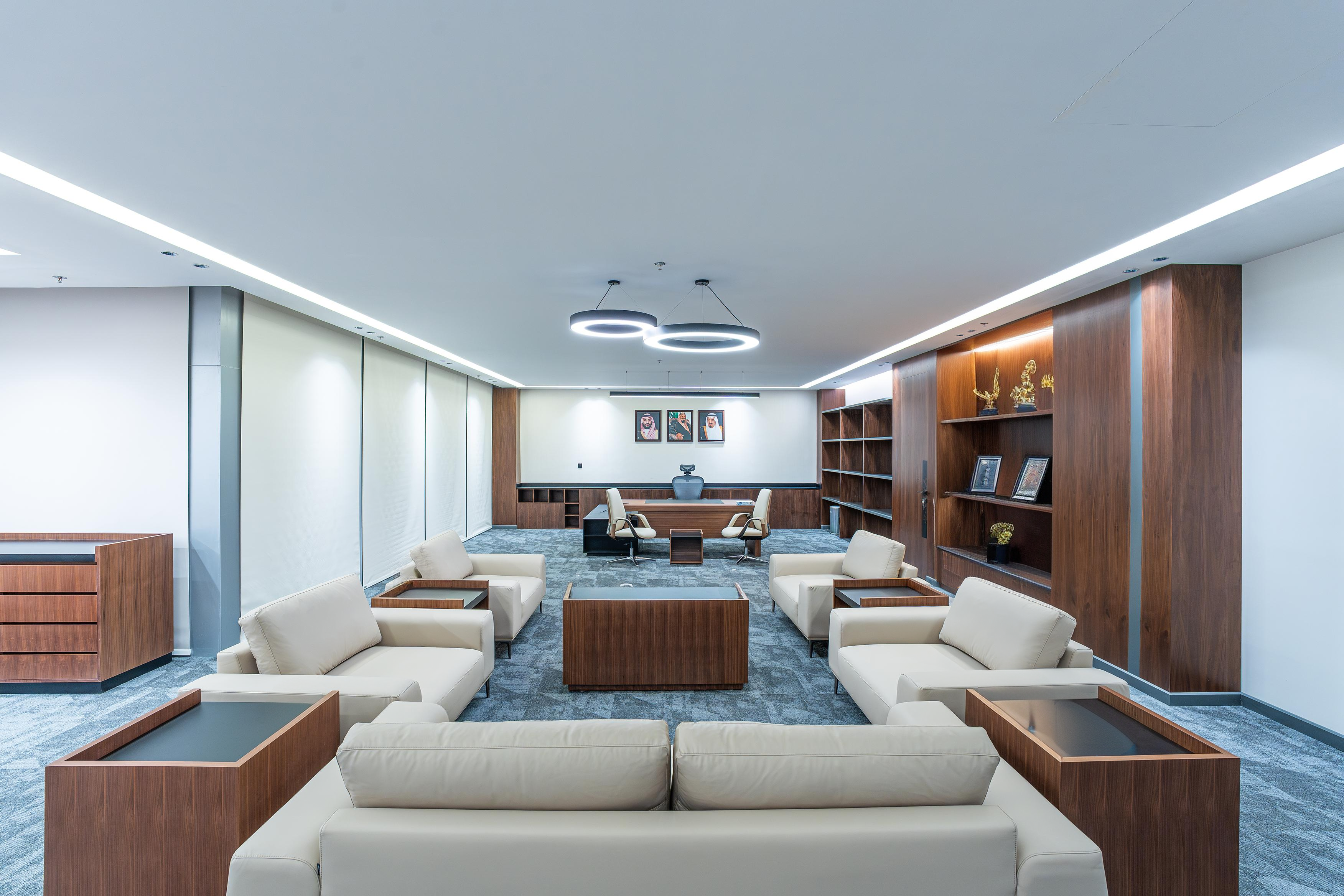 Modern office lounge with beige sofas, wooden tables, and bookshelves by top furniture supplier in Riyadh – صالة مكتب عصرية تحتوي على كنبات بيج وطاولات خشبية ورفوف كتب من أفضل مورّد أثاث مكتبي في الرياض