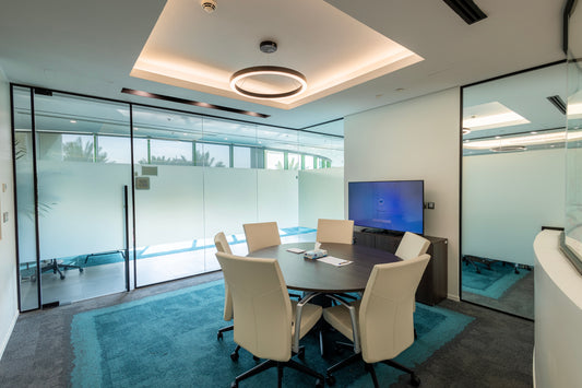 Modern meeting room with round wooden table, leather chairs, glass walls, and screen by Atelier 21 KSA – مفن الرسام, top office furniture supplier and interior designer in Riyadh, Saudi Arabia – غرفة اجتماعات حديثة تحتوي على طاولة خشبية دائرية، كراسي جلدية، جدران زجاجية، وشاشة من مفن الرسام، أفضل مورد أثاث مكتبي وأفضل مصمم داخلي في الرياض، السعودية 8