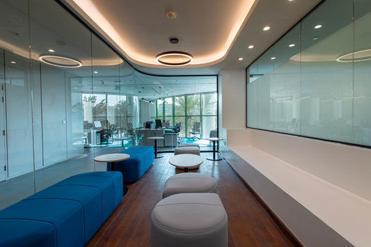 Modern office lounge with blue and gray seating, glass partitions, and round tables by Atelier 21 KSA – مفن الرسام, top office furniture supplier and top interior designer in Riyadh, Saudi Arabia – صالة مكتبية حديثة تحتوي على مقاعد زرقاء ورمادية، طاولات دائرية، وفواصل زجاجية من مفن الرسام، أفضل مورد أثاث مكتبي وأفضل مصمم داخلي في الرياض، السعودية 9