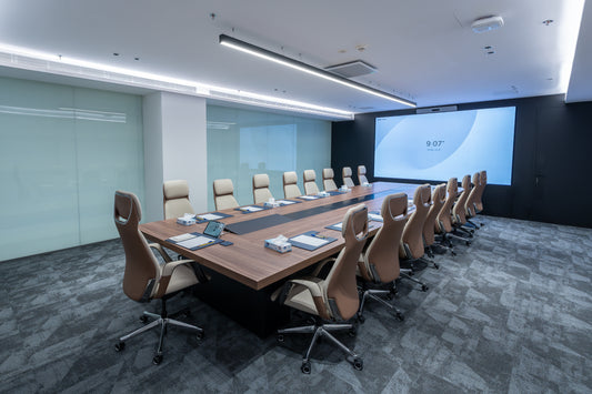 Modern conference room with a long wooden table and beige chairs, featuring a large screen on the wall by Atelier 21 KSA, top office furniture supplier in Riyadh – غرفة اجتماعات عصرية تحتوي على طاولة خشبية طويلة وكراسي بيج، مع شاشة كبيرة على الحائط من مفن الرسام، أفضل مورّد أثاث مكتبي في الرياض 4