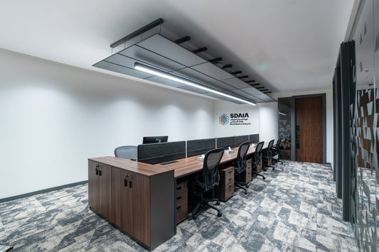 Modern office setup with wooden desks and chairs in a well-lit room by Atelier 21 KSA, top office furniture supplier in Riyadh – إعداد مكتب عصري يحتوي على مكاتب وكراسي خشبية في غرفة مضاءة جيدًا من مفن الرسام، أفضل مورّد أثاث مكتبي في الرياض 10