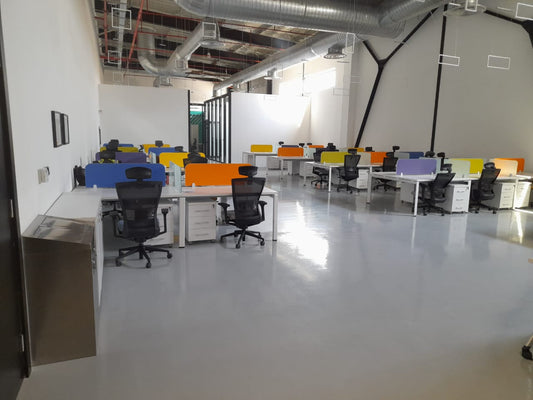 Modern open-plan office at Misk Foundation in Riyadh, featuring ergonomic black mesh chairs, white desks, and colorful divider panels in orange, blue, purple, green, and yellow. The polished white epoxy flooring reflects natural light, enhancing the bright and vibrant workspace. Industrial exposed ceiling with ducts adds a contemporary touch. مساحة عمل مرنة ومُبهجة تعكس روح الإبداع والابتكار في مؤسسة مسك بالرياض. 9