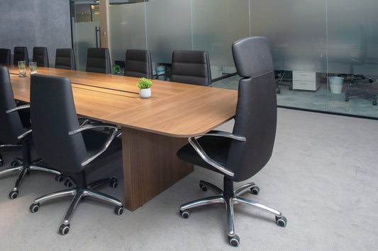 Modern conference room with long wooden meeting table, black leather chairs, indoor plants, and wall-mounted screen by Atelier 21 KSA, top office furniture supplier in Riyadh – غرفة اجتماعات عصرية تحتوي على طاولة اجتماعات خشبية طويلة، كراسي جلدية سوداء، نباتات داخلية، وشاشة مثبتة على الحائط من تصميم مفن الرسام، أفضل مورّد أثاث مكتبي في الرياض 21
