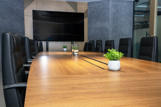 Modern conference room with long wooden meeting table, black leather chairs, indoor plants, and wall-mounted screen by Atelier 21 KSA, top office furniture supplier in Riyadh – غرفة اجتماعات عصرية تحتوي على طاولة اجتماعات خشبية طويلة، كراسي جلدية سوداء، نباتات داخلية، وشاشة مثبتة على الحائط من تصميم مفن الرسام، أفضل مورّد أثاث مكتبي في الرياض 20