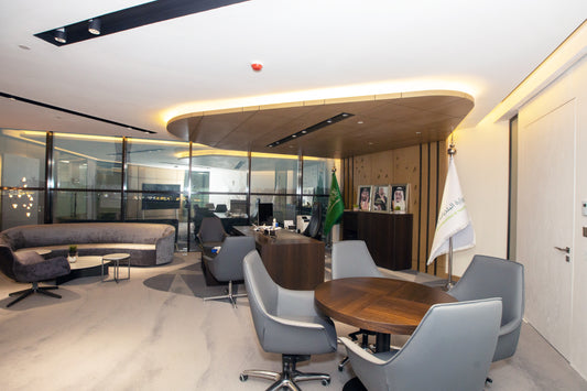 Modern executive office featuring custom wood ceiling, round meeting table, grey leather chairs, curved velvet sofa, and Ministry of Municipal and Rural Affairs branding – designed by Atelier 21 KSA, expert in luxury office interiors in Saudi Arabia – مكتب تنفيذي عصري بتصميم سقف خشبي مميز، طاولة اجتماعات دائرية، كراسي جلدية رمادية، أريكة مخملية منحنية، وهوية وزارة الشؤون البلدية والقروية، من تنفيذ مفن الرسام، المتخصص في تصاميم المكاتب الفاخرة في السعودية 26
