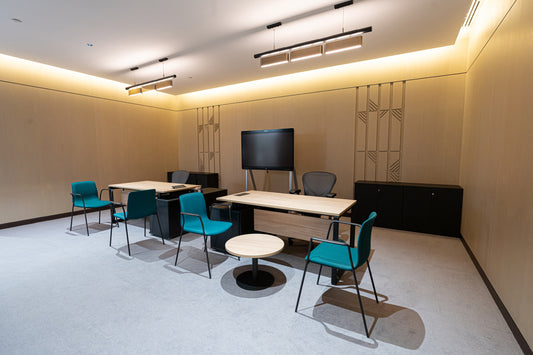 Modern office workspace with wooden desks, ergonomic chairs, teal guest seating, and a large screen display by Atelier 21 KSA, top office furniture supplier and interior designer in Saudi Arabia – مساحة عمل مكتبية عصرية تحتوي على مكاتب خشبية، كراسي مريحة، كراسي ضيوف باللون الفيروزي، وشاشة عرض كبيرة من تصميم مفن الرسام، أفضل مورّد أثاث ومصمم داخلي في السعودية 23