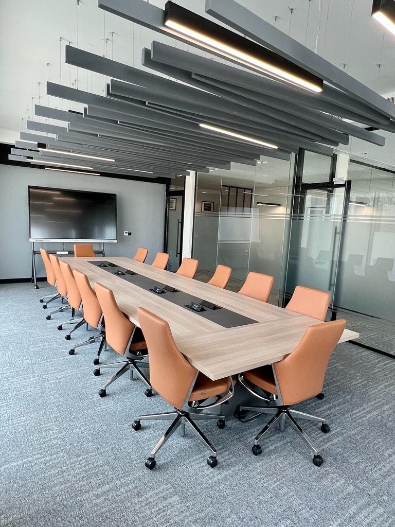 Contemporary boardroom interior featuring rich leather executive chairs, a sleek black conference table, and ceiling acoustic panels, designed by Atelier 21 KSA – Top Interior Designer and Office Furniture Supplier in Saudi Arabia and Riyadh. تصميم داخلي لغرفة اجتماعات عصرية تضم كراسي تنفيذية جلدية وطاولة سوداء أنيقة وسقف بمعالجة صوتية من تنفيذ مفن الرسام، مما يعكس تميز مفن الرسام كأفضل مصمم داخلي ومورد أثاث ومصمم مكاتب في السعودية والرياض.