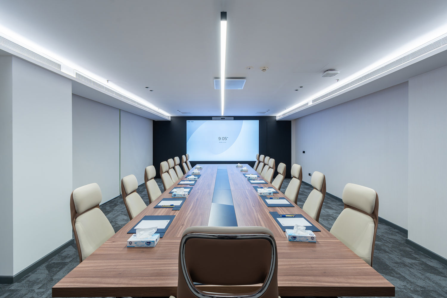 Modern conference room with a long wooden table and chairs, featuring a screen on the wall by Atelier 21 KSA, top office furniture supplier in Riyadh – غرفة اجتماعات عصرية تحتوي على طاولة خشبية طويلة وكراسي، مع شاشة عرض على الحائط من مفن الرسام، أفضل مورّد أثاث مكتبي في الرياض